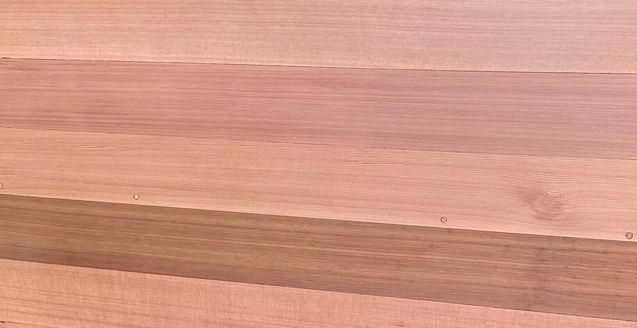 Western red cedar boards in clear vertical grain, showing straight grain and noticeable color variation from pale pink to reddish brown between boards